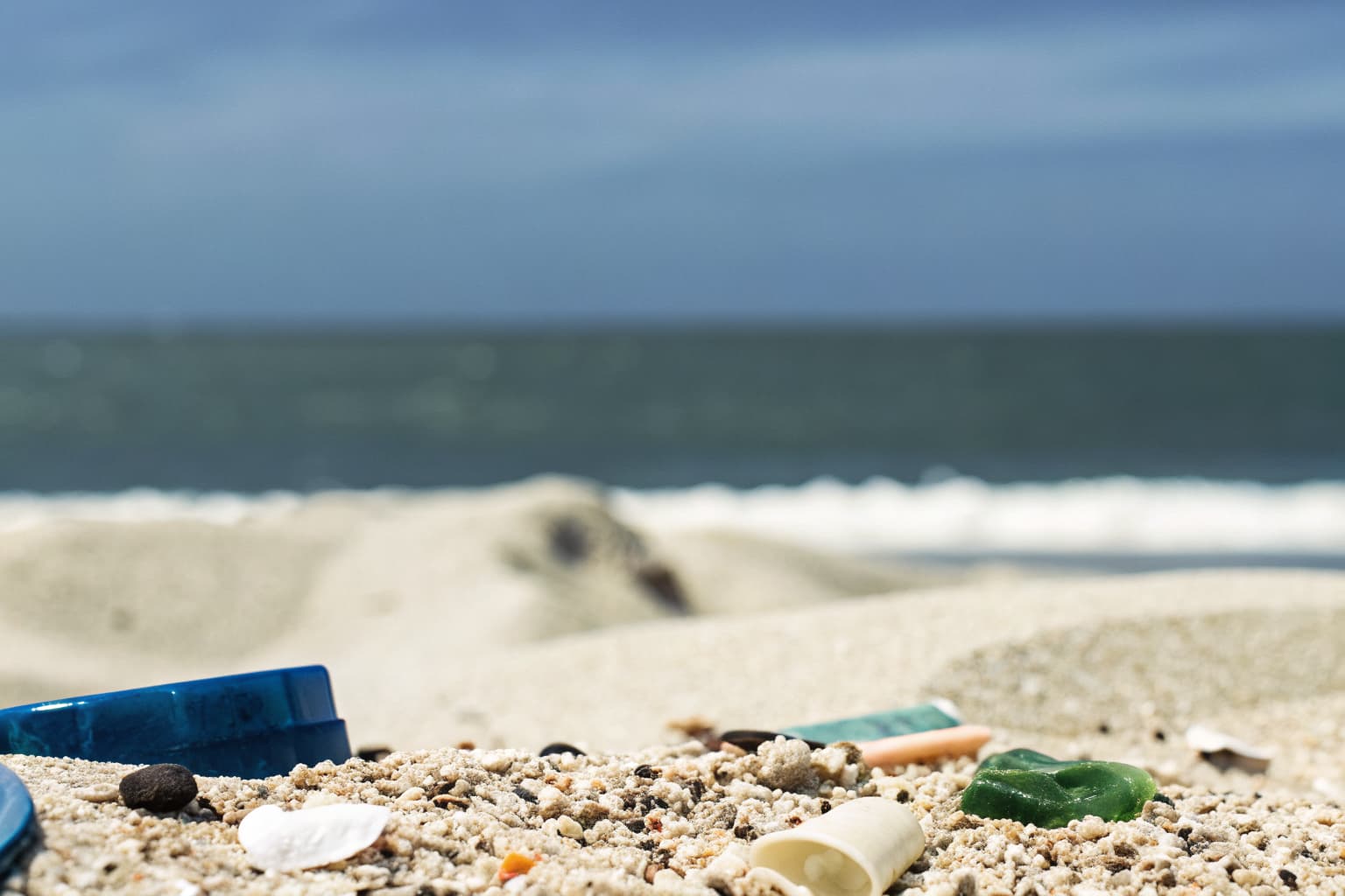 Weathered plastic fragments mixed into coastal beach sand near the ocean's edge