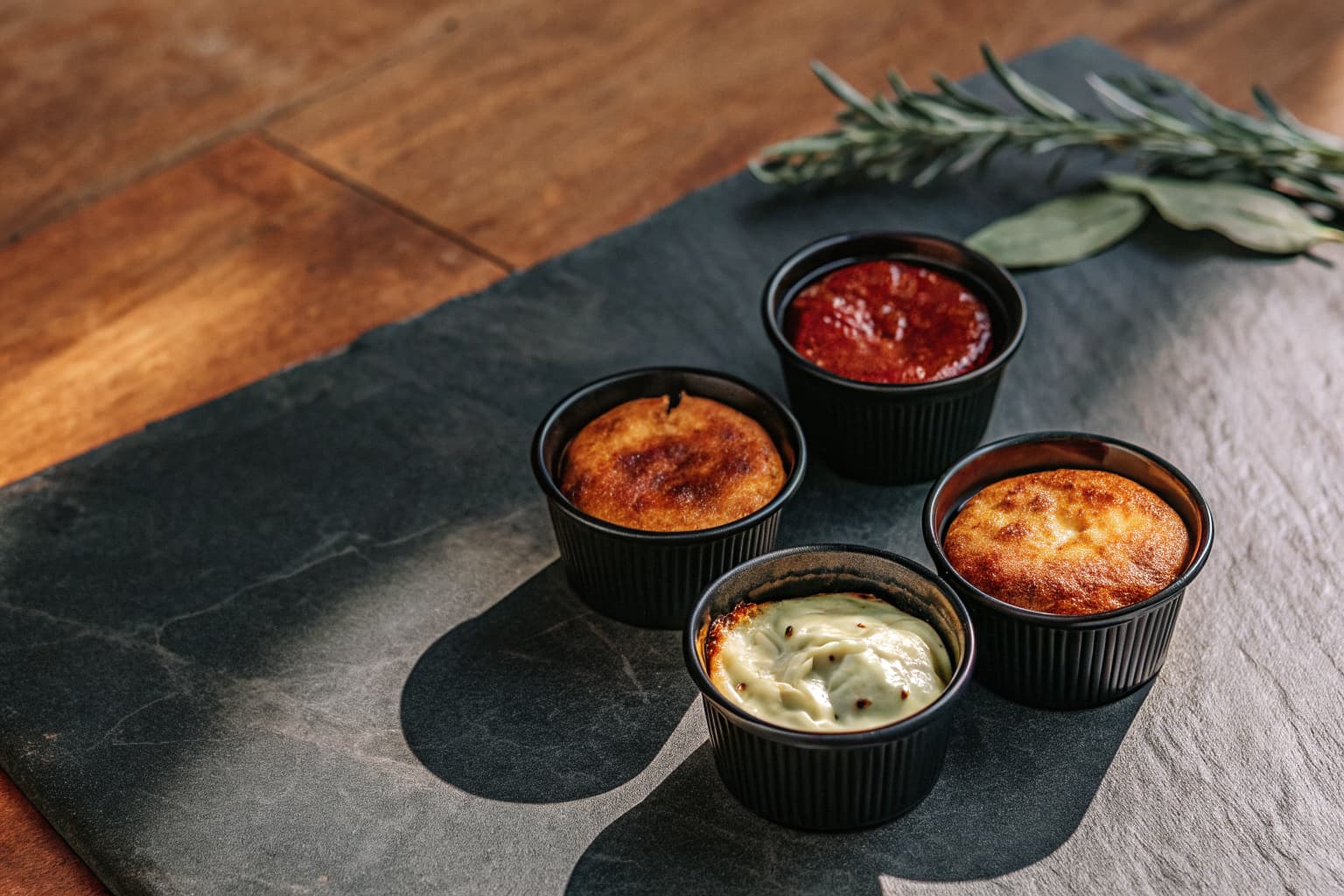 Small black souffle portion cups filled with sauces and dressings on a dark slate surface — sustainable condiment packaging by Pure Form Solution