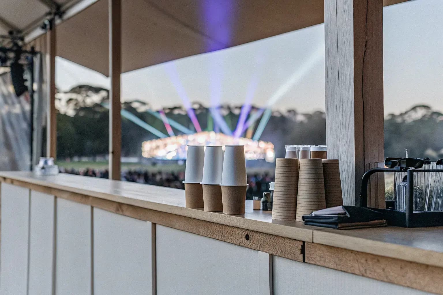 Concert venue concession stand with compostable cups and eco-friendly serviceware, stage lights in background