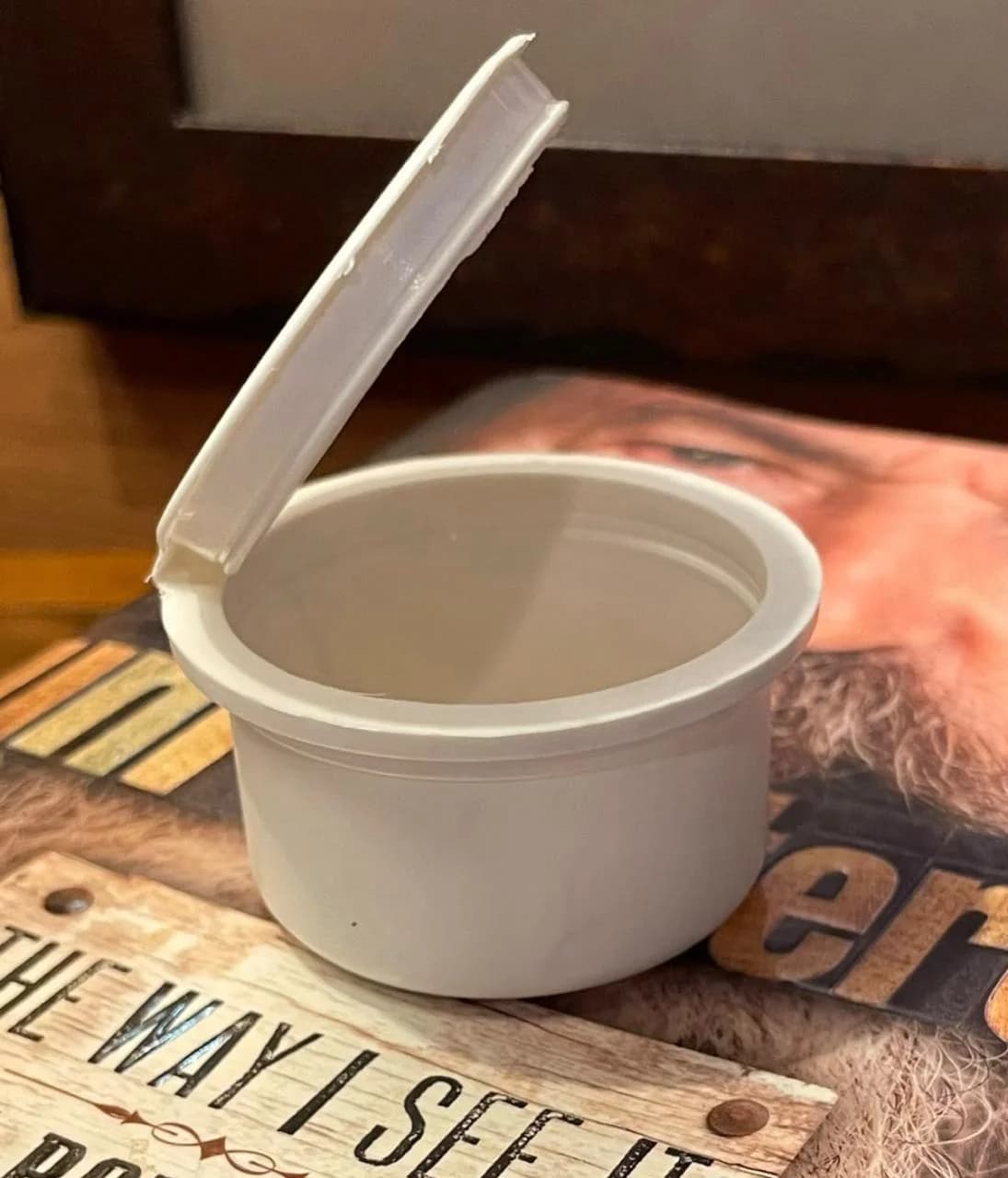 Biodegradable PHA pop top container with hinged flip-top lid open, resting on a wooden surface — sustainable edibles packaging by Pure Form Solution